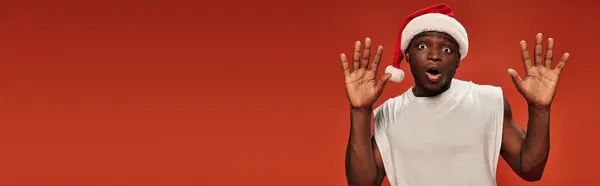 Испуганный африканский американец в шляпе Санты показывает стоп-жест с открытым ртом на красном, баннер — стоковое фото