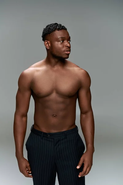 Shirtless african american man with muscular body posing in black pants and looking away on grey — Stock Photo