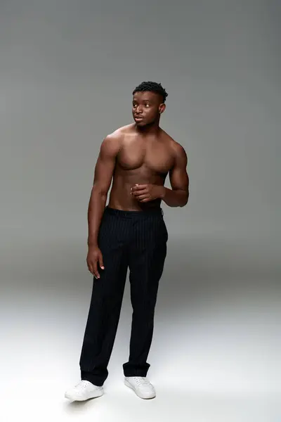 Comprimento total de homem americano Africano muscular e sem camisa em calças pretas olhando para longe em cinza — Fotografia de Stock