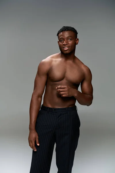 Positive african american fitness model with shirtless torso looking at camera on grey backdrop — Stock Photo