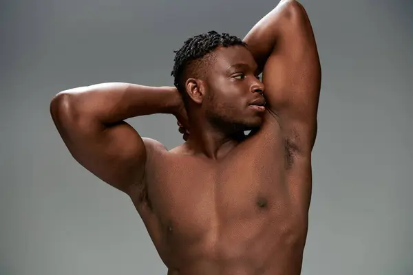 Sportivo e senza maglietta uomo africano americano con corpo muscolare posa con le mani dietro la testa sul grigio — Foto stock