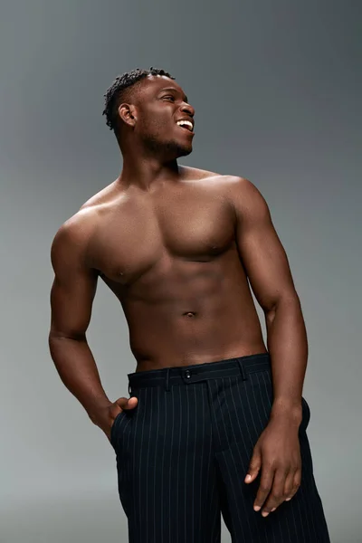Homem americano africano alegre com corpo muscular sem camisa e mão no bolso olhando afastado no cinza — Fotografia de Stock