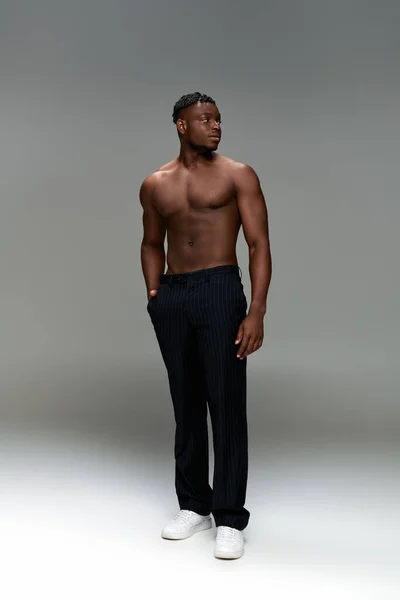 Sportlicher afrikanisch-amerikanischer Mann mit kräftigem Körper und einer Hand in der Hosentasche, der wegschaut auf grau, volle Länge — Stockfoto