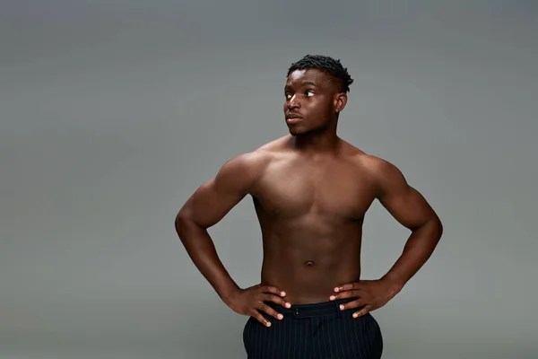 Confiado hombre afroamericano fuerte torso posando con las manos en las caderas en gris, modelo de fitness - foto de stock