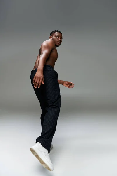 Hemdlos und stark afrikanisch-amerikanischer Typ in schwarzer Hose schaut in die Kamera, während er auf grau posiert — Stockfoto
