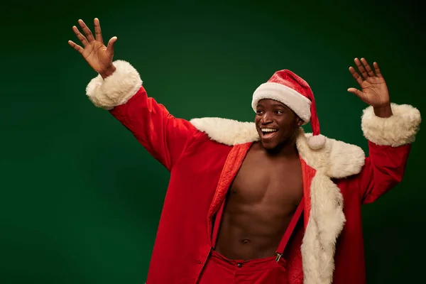 Joyful african american guy in christmas costume on shirtless body waving hands on green backdrop — Stock Photo