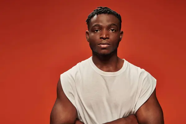 Confident athletic african american man in white tank top looking at camera on red studio backdrop — Stock Photo