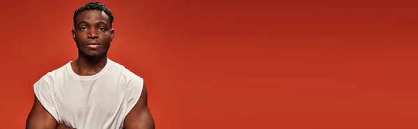 Confident dark skinned man in white tank top looking at camera on red studio backdrop, banner — Stock Photo