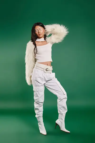 Brunette asian woman in total white outfit and makeup posing on green backdrop, winter fashion — Stock Photo