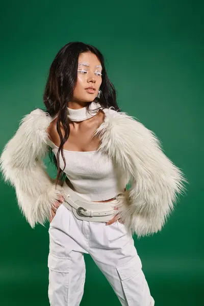 Asiatique brunette femme en total blanc tenue et maquillage posant avec les mains sur les hanches sur fond vert — Photo de stock