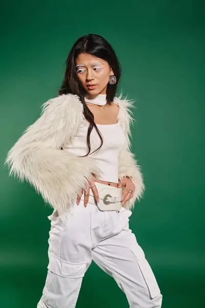 Азіатська брюнетка жінка в загальному білому вбранні і макіяж позує на зеленому тлі, зимова мода — стокове фото