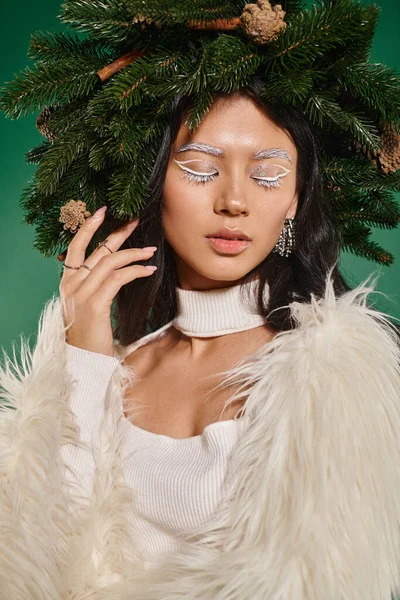 Winterkonzept, junge Frau mit weißem Eyeliner und geschlossenen Augen posiert im Kranz vor grünem Hintergrund — Stockfoto