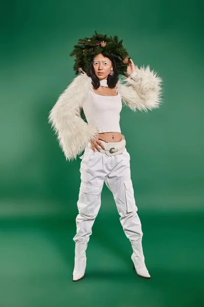 Moda invernale, bella donna con trucco bianco e vestito alla moda in posa in ghirlanda su sfondo verde — Foto stock