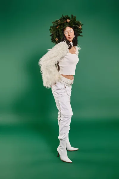 Época festiva, mulher asiática com maquiagem branca e roupa na moda posando em grinalda no fundo verde — Fotografia de Stock
