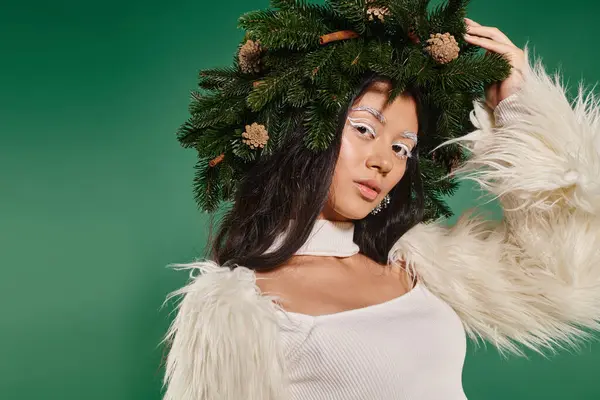 Weihnachtszeit, hübsche Frau mit weißem Make-up und Winteroutfit posiert im Kranz vor grünem Hintergrund — Stockfoto