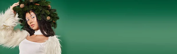 Festbanner, asiatische Frau mit weißem Make-up und Winteroutfit posiert im Kranz vor grünem Hintergrund — Stockfoto