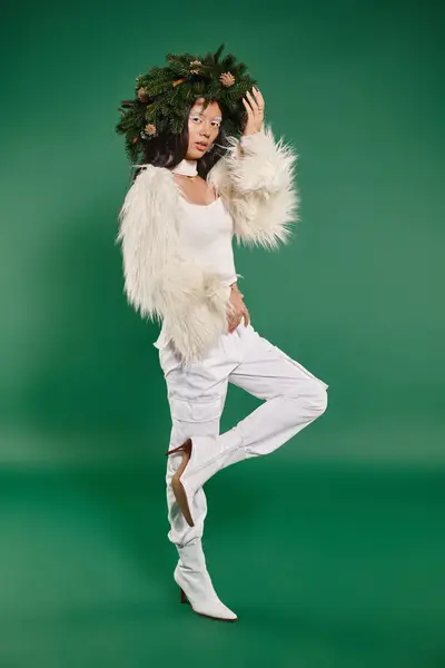 Святковий сезон, азіатська жінка з білим макіяжем і модним вбранням позує у вінок на зеленому тлі — стокове фото