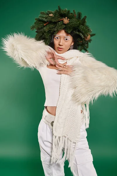 Stagione festiva, bruna donna asiatica con trucco bianco e vestito alla moda in posa in ghirlanda sul verde — Foto stock