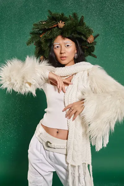 Зимняя мода, молодая женщина с натуральным венком позирует в белой стильной одежде под падающим снегом — стоковое фото