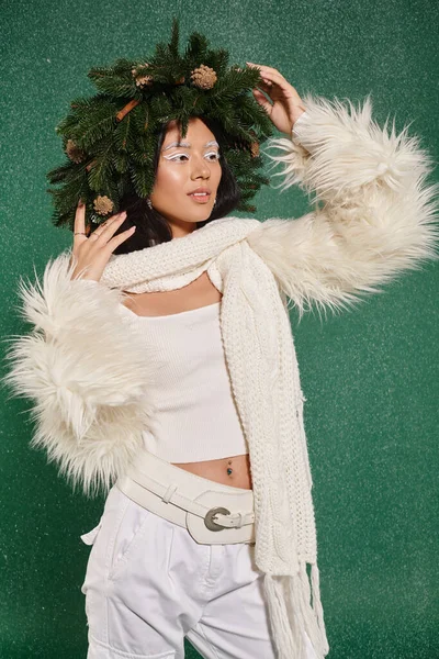 Moda de invierno, mujer bonita con corona natural posando en ropa blanca y elegante bajo la nieve que cae - foto de stock