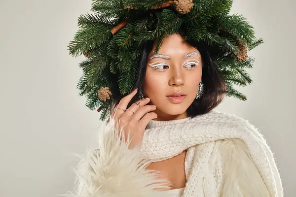 Belleza de invierno, mujer atractiva con corona de pino natural posando en ropa blanca sobre fondo gris - foto de stock