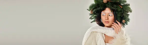 Belleza de invierno, mujer atractiva con corona de pino natural posando en ropa blanca en gris, bandera - foto de stock