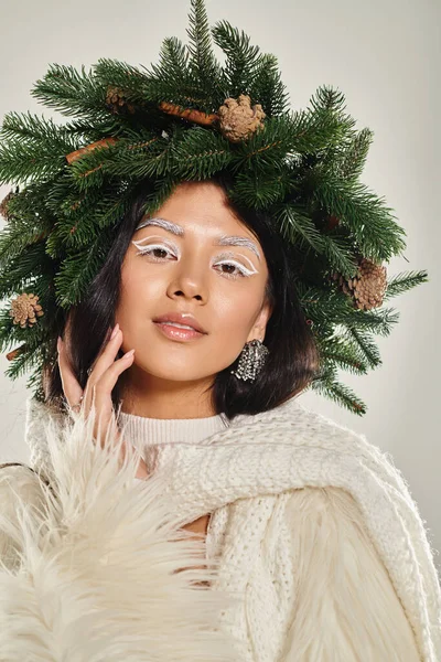 Belleza de invierno, mujer atractiva con corona de pino verde posando en ropa blanca sobre fondo gris — Stock Photo