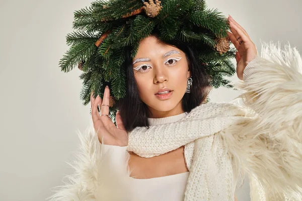 Belleza de invierno, mujer encantada con corona de pino natural posando en ropa blanca sobre fondo gris - foto de stock