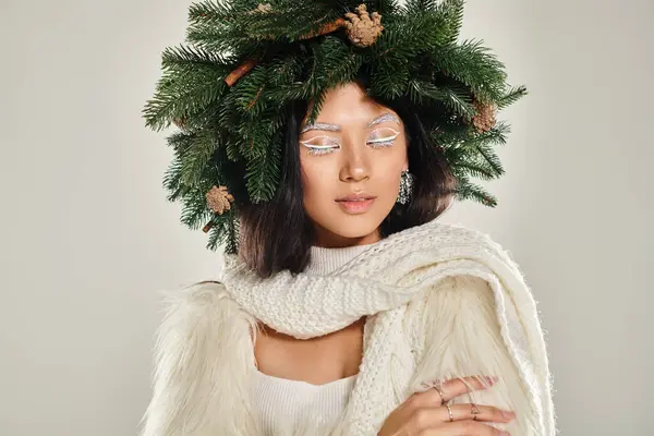 Belleza de invierno, mujer encantadora con corona de pino natural posando en ropa blanca sobre fondo gris - foto de stock