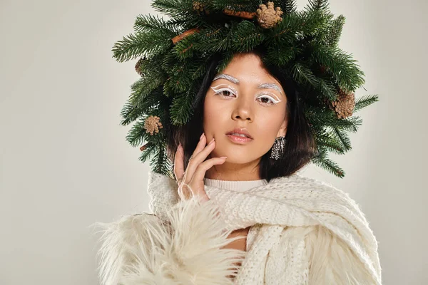 Belleza asiática, mujer seductora con corona de pino natural posando en ropa blanca sobre fondo gris - foto de stock