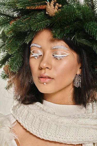 Winter trends, close up of asian woman with white eye makeup and beads on face posing in wreath — Stock Photo