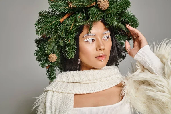 Winter trends, beautiful woman with white eye makeup and beads on face posing in wreath on grey — Stock Photo