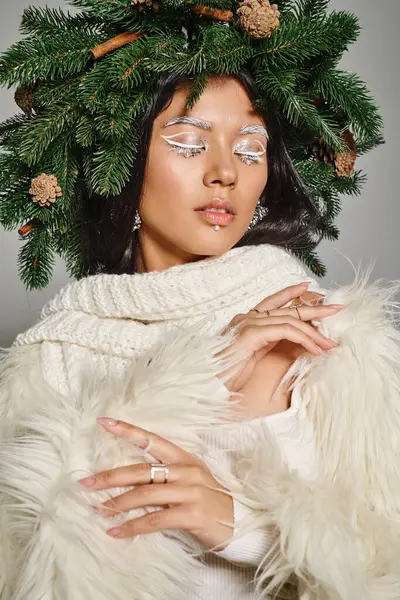 Holiday style, attractive woman with white eye makeup and beads on face posing in wreath on grey — Stock Photo