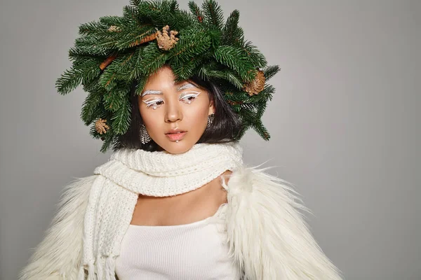 Charming winter queen with white eye makeup and beads on face posing in wreath on grey background — Stock Photo