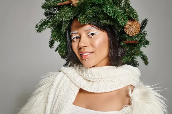 Mujer feliz con maquillaje de ojos blancos y cuentas en la cara posando en corona sobre fondo gris, reina de invierno - foto de stock