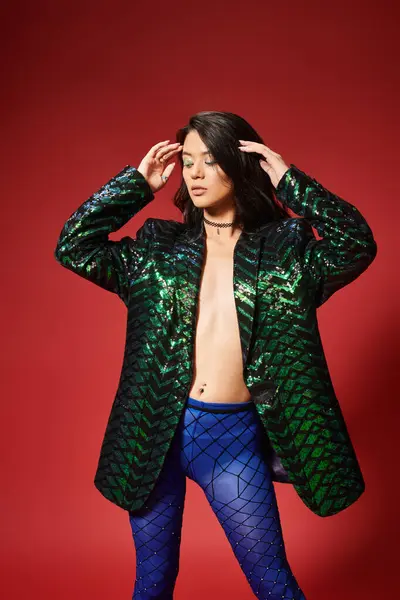 Сексуальная азиатка в стильной зеленой куртке с блестками и синими колготками позирует на красном фоне — стоковое фото