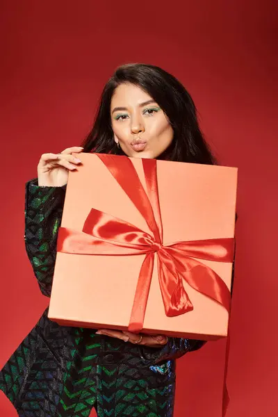 Asian woman in green jacket with sequins holding wrapped gift box and sending air kiss on Christmas — Stock Photo