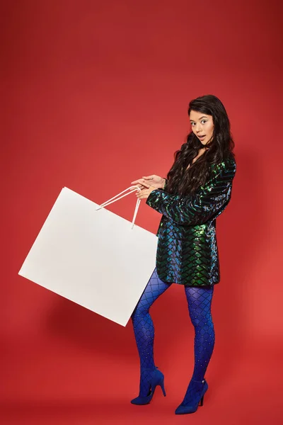 Black friday concept, asian woman in green jacket with sequins holding huge shopping bag on red — Stock Photo