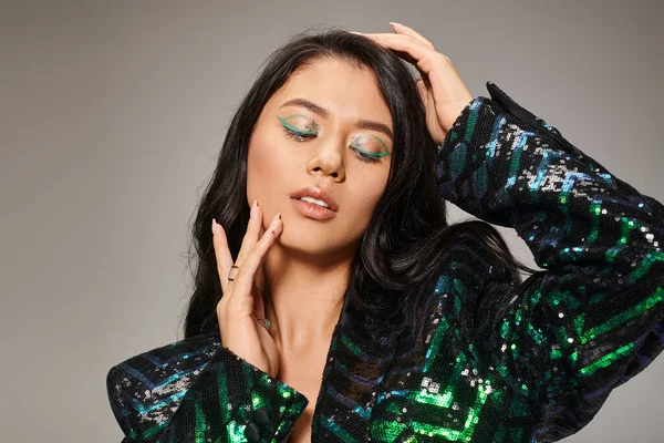 Beautiful asian woman in green jacket with sequins and bold eye makeup posing on grey backdrop — Stock Photo