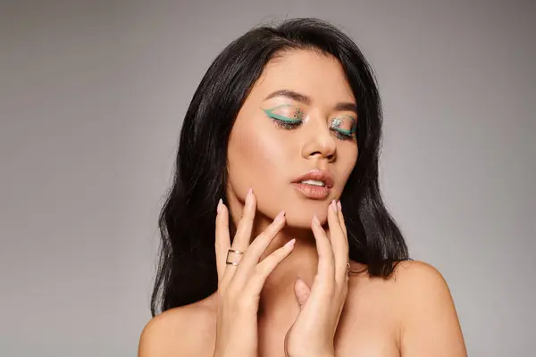 Attractive asian woman with green eyeliner and bare shoulders posing on grey background, bold makeup — Stock Photo