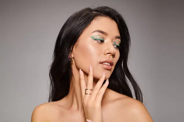 Brunette asiatique femme avec eye-liner vert et les épaules nues posant sur fond gris, audacieux maquillage — Photo de stock