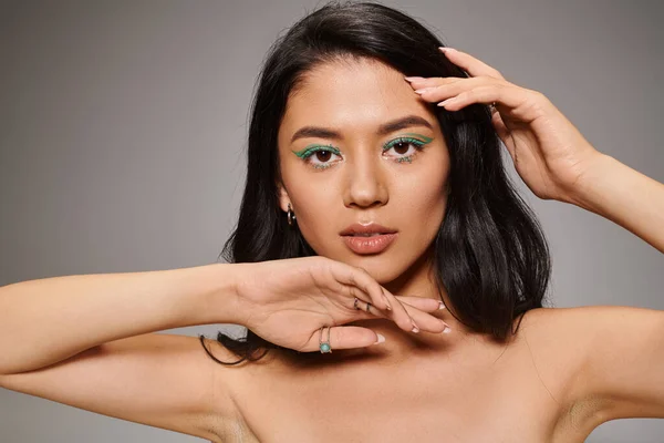 Schöne asiatische Frau mit schimmernden grünen Augen Make-up und nackten Schultern posiert auf grauem Hintergrund — Stockfoto