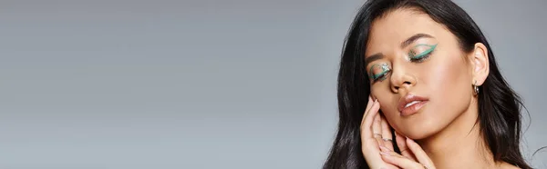 Woman with shimmery green makeup and bare shoulders posing with hands near face on grey, banner — Stock Photo