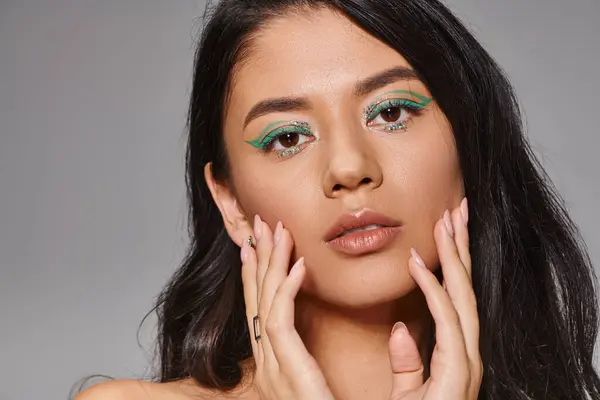 Pretty woman with green makeup and bare shoulders posing with hands near face on grey background — Stock Photo