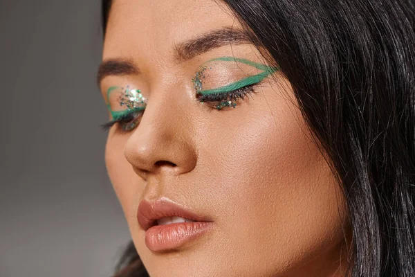 Close up of beautiful asian woman with brunette hair and shiny eye makeup on grey background — Stock Photo