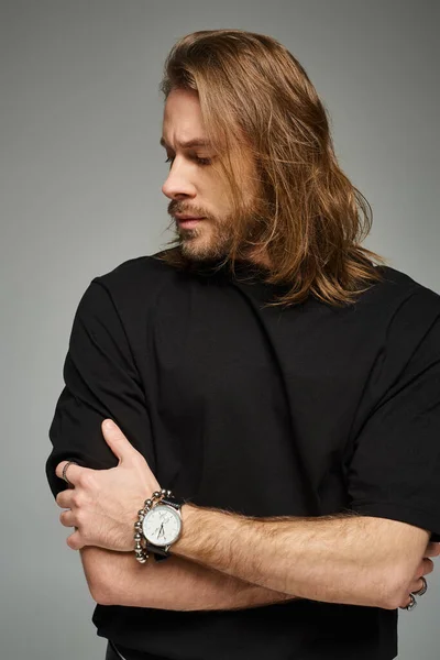 Homme barbu et beau aux cheveux longs posant en t-shirt noir et jean sur fond gris — Photo de stock
