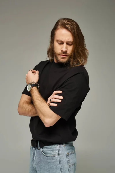 Portrait of bearded and good looking man with long hair posing in jeans and t-shirt on grey backdrop — Stock Photo
