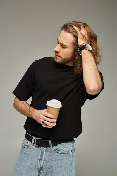Handsome man with long hair and beard holding paper cup with coffee to go on grey background — Stock Photo