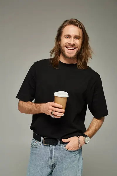 Happy man with long hair and beard holding paper cup with coffee to go on grey background — Stock Photo