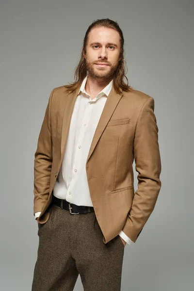 Geschäftsmann mit Bart und langen Haaren posiert mit den Händen in der Tasche vor grauem Hintergrund, formelle Kleidung — Stockfoto